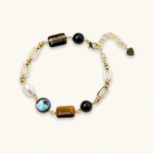 Gold chain bracelet with tiger's eye, obsidian, pearl, and iridescent abalone stones on cream background.