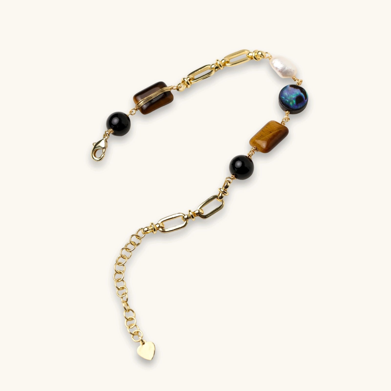 Gold chain bracelet with tiger's eye, obsidian, pearl, and iridescent abalone stones on cream background.